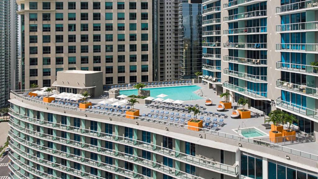 Vista aérea de uma área de piscina na cobertura do Hyatt Centric Brickell Miami com espreguiçadeiras e guarda-sóis em um edifício moderno e curvo em um ambiente urbano.