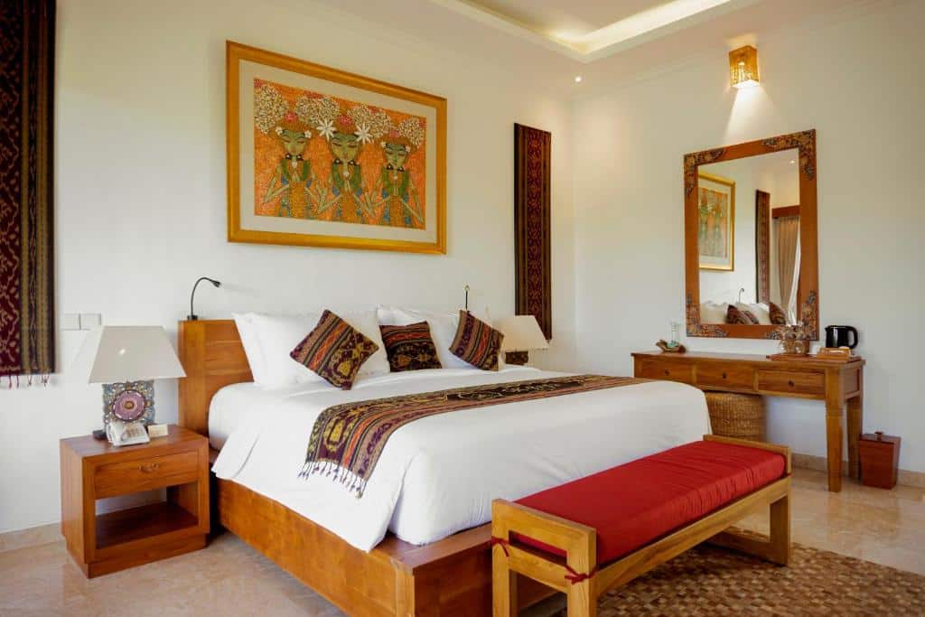 Um quarto aconchegante do GK Bali Resort com uma cama de casal, almofadas coloridas, um espelho grande, móveis de madeira e uma pintura decorativa na parede. Representa onde ficar em Bali.