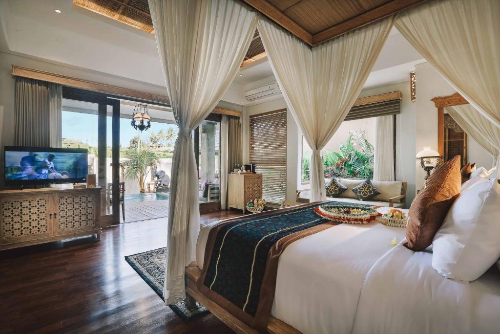 Quarto luxuoso do Kuwarasan A Pramana Experience com cama de dossel, piso de madeira, cortinas abertas, TV e vista para a piscina privativa e o jardim externo. Representa onde ficar em Bali.
