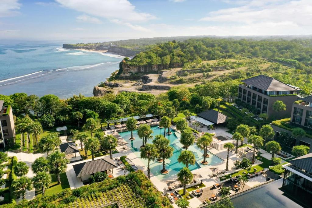 Vista aérea de um resort Radisson Blu Bali Uluwatu com várias piscinas, cercado por vegetação exuberante e falésias oceânicas sob um céu parcialmente nublado. Representa onde ficar em Bali.