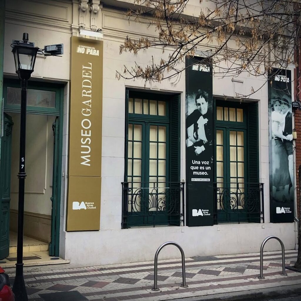 Fachada do Museo Gardel, um dos pontos turísticos de Buenos Aires, com faixas e portas verdes. Uma árvore com galhos nus está na frente em uma calçada de ladrilhos.