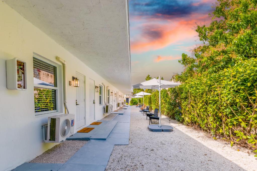 Uma fileira de quartos da Casa Agave By Renzzi com portas e janelas de frente para um caminho de cascalho ladeado por vegetação. Cadeiras de estar e guarda-sóis estão à direita.