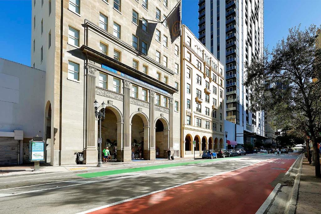 Vista da rua do edifício do Eurostars Langford com vários andares com entradas em arco, estruturas altas adjacentes e uma faixa de ônibus vermelha em primeiro plano.