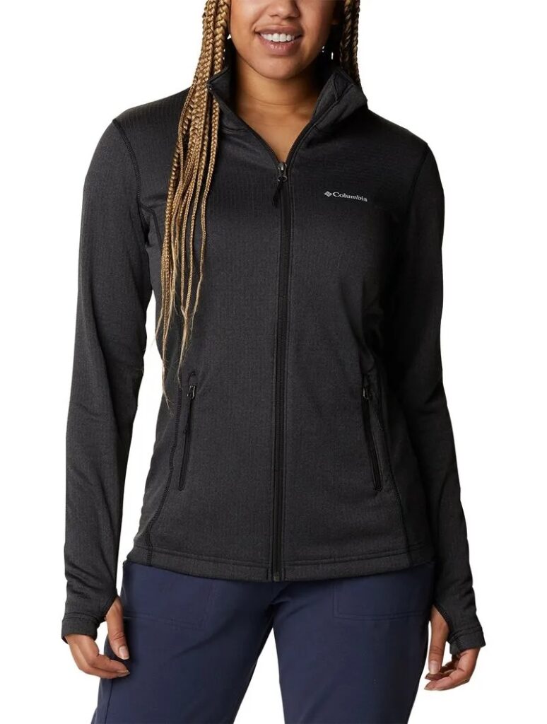Uma pessoa vestindo uma jaqueta preta com zíper e um logotipo no peito e calças azul-marinho, em pé, contra um fundo branco. Essa é a Jaqueta Fleece Columbia Feminina Park View.