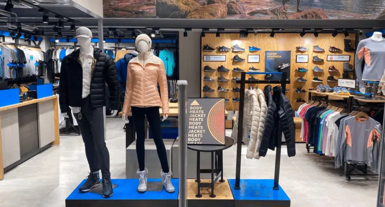 Uma vitrine da Loja Columbia Shopping da Barra com manequins vestidos com roupas esportivas, jaquetas e sapatos. Prateleiras de vestuário são visíveis ao fundo. Essa é uma das lojas Columbia no Brasil.