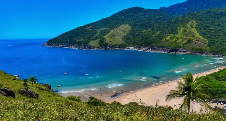 Vista do Mirante do Bonete com águas cristalinas azul-turquesa, cercada por colinas verdejantes sob um céu azul brilhante. Imagem para ilustrar post sobre melhores praias de Ilhabela.
