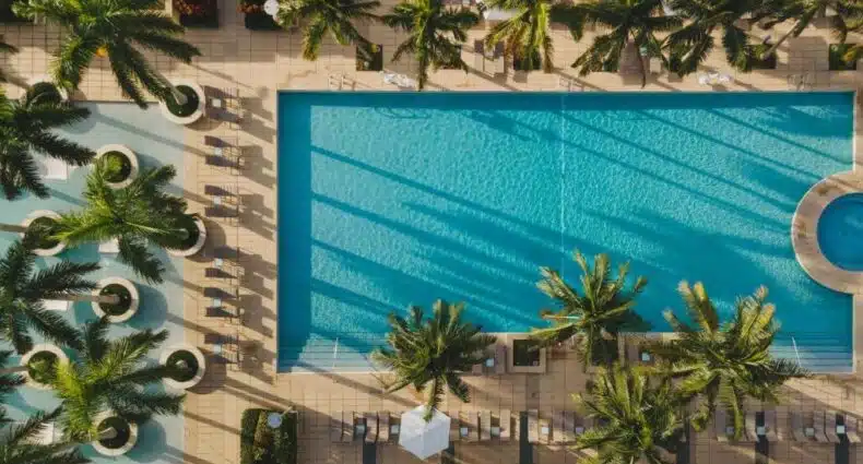 Vista aérea de uma grande piscina retangular do Four Seasons Hotel Miami cercada por palmeiras, espreguiçadeiras e piscinas circulares menores. Representa hotéis em Brickell.