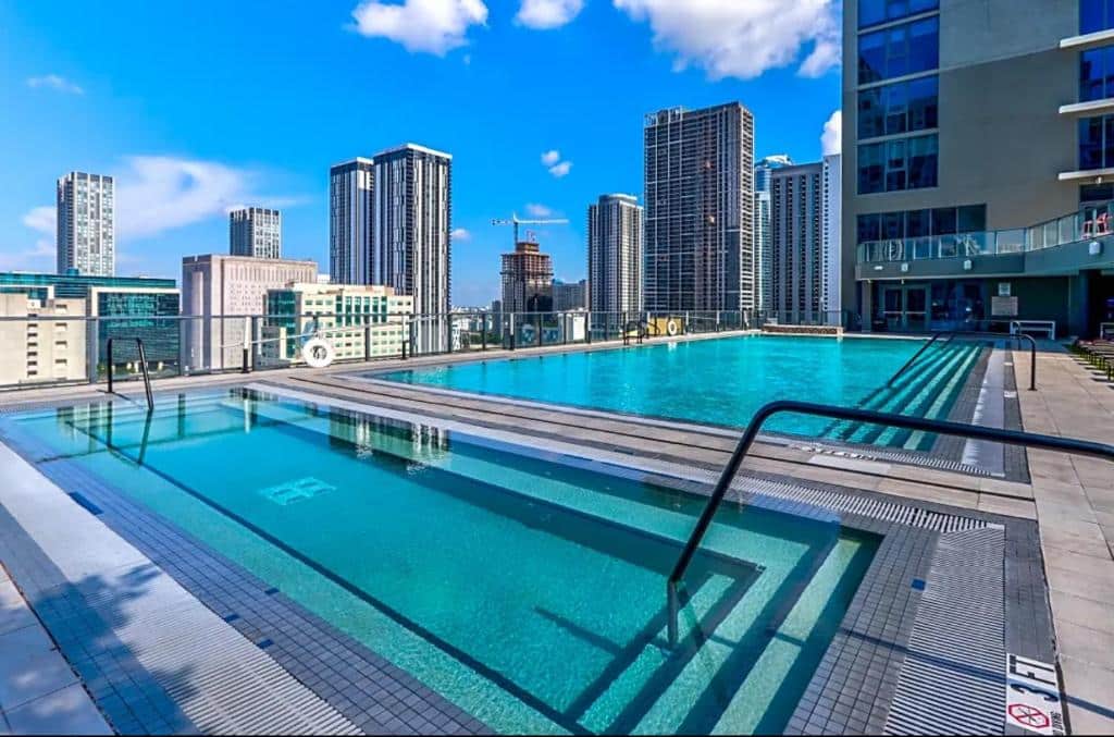 Piscina na cobertura do Luxurious King Bed Suite in Downtown Miami com arranha-céus da cidade ao fundo, sob um céu azul com nuvens dispersas.