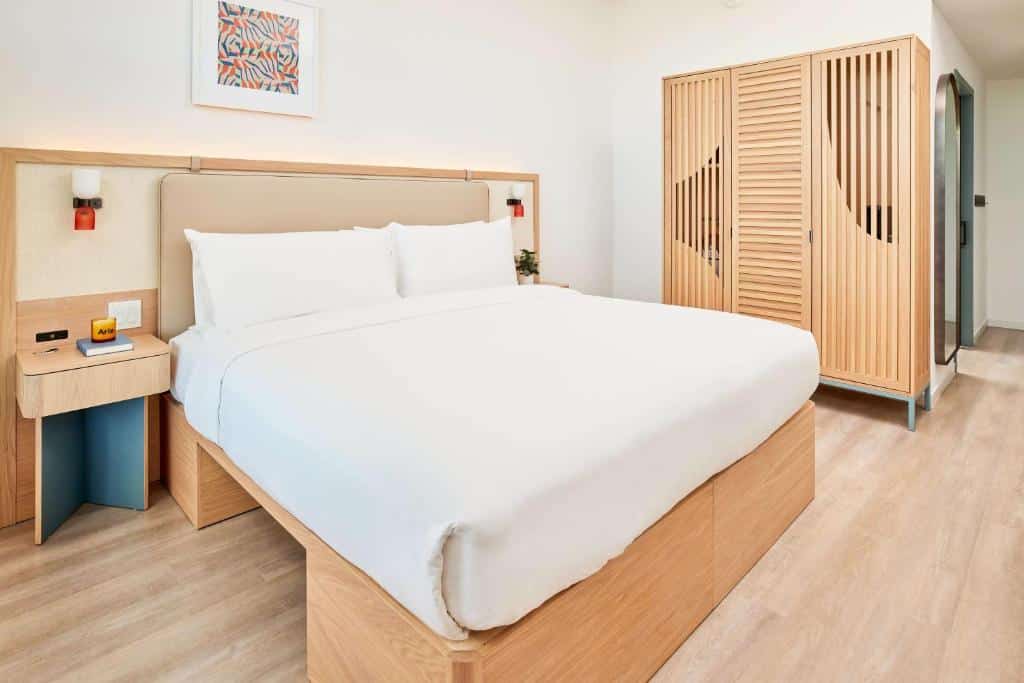 Um quarto do Arlo Wynwood Miami com uma cama grande, móveis de madeira, um guarda-roupa e uma pequena mesa de cabeceira com um abajur de parede acima dela.