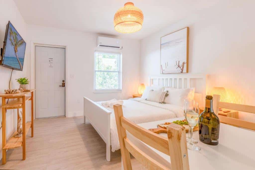 Um quarto minimalista do Casa Agave By Renzzi com uma cama, mesa de madeira, TV na parede, luminária de teto e duas taças de vinho branco na mesa. Representa onde ficar em Miami.