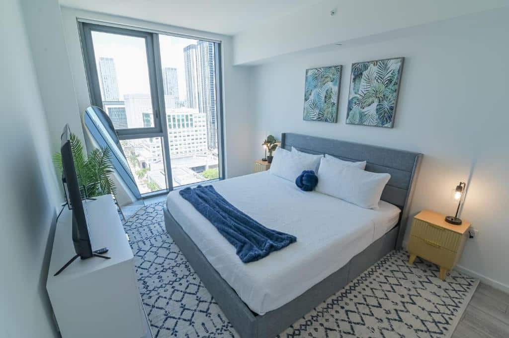 Um quarto do Luxurious King Bed Suite in Downtown Miami com uma cama grande, detalhes em azul, uma TV e uma janela com vista para a cidade lá fora.