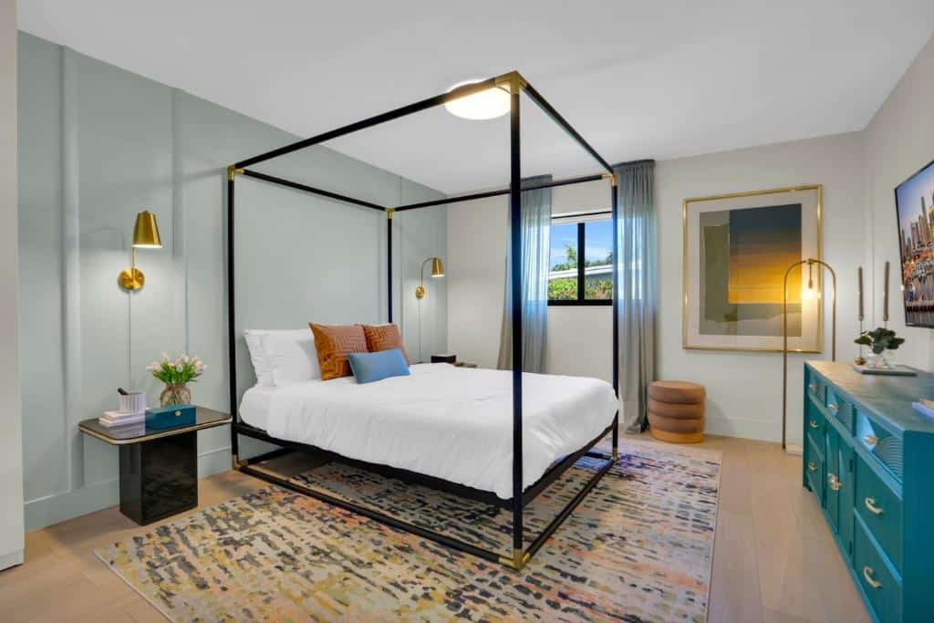 Quarto do Miami GEM com uma cama de dossel preta, roupa de cama branca, travesseiros coloridos, uma cômoda azul e obras de arte abstrata na parede. Representa onde ficar em Miami.
