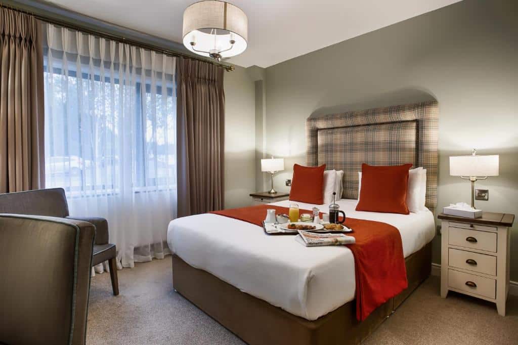 Quarto do Glenside Hotel com uma cama de casal, roupa de cama vermelha e branca, duas mesas de cabeceira com luminárias, uma cadeira e uma bandeja com itens de café da manhã.