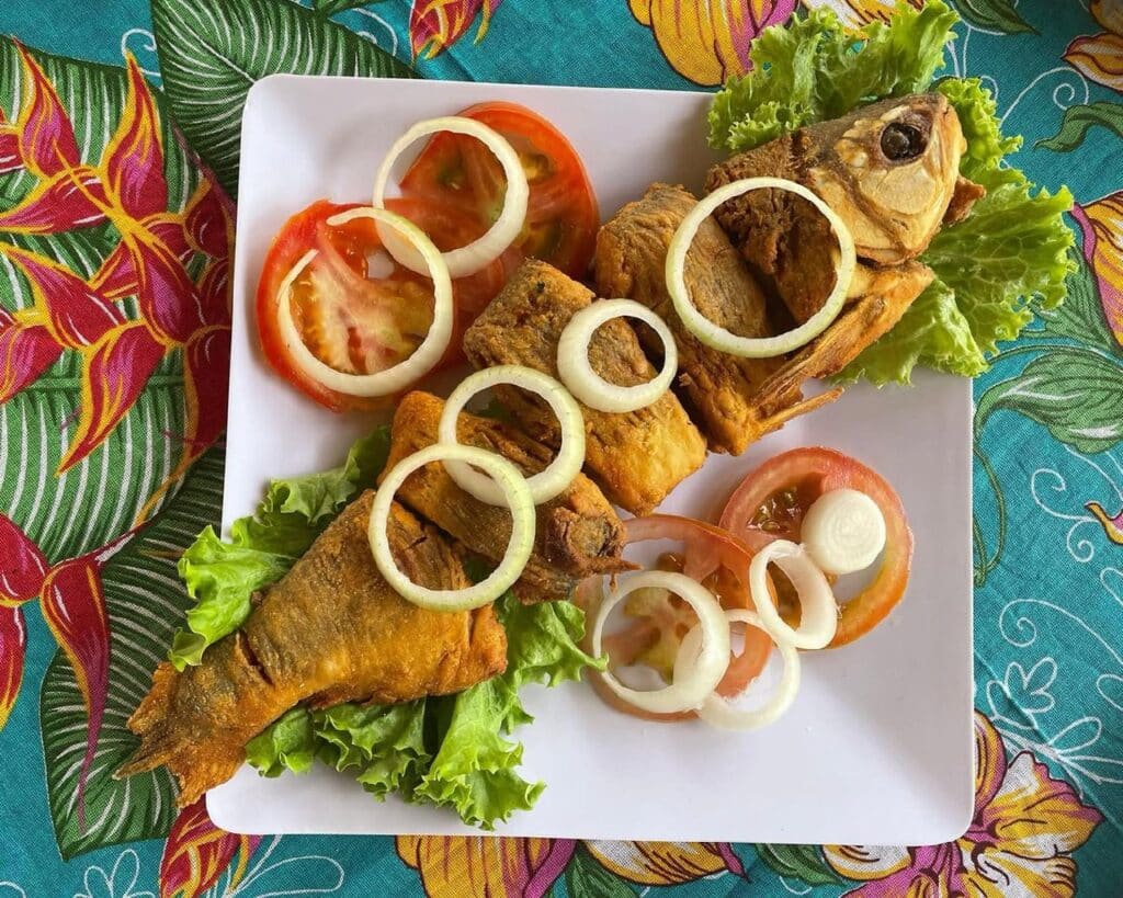 Prato no Restaurante Pé na Areia com peixe frito guarnecido com anéis de cebola, fatias de tomate e alface.