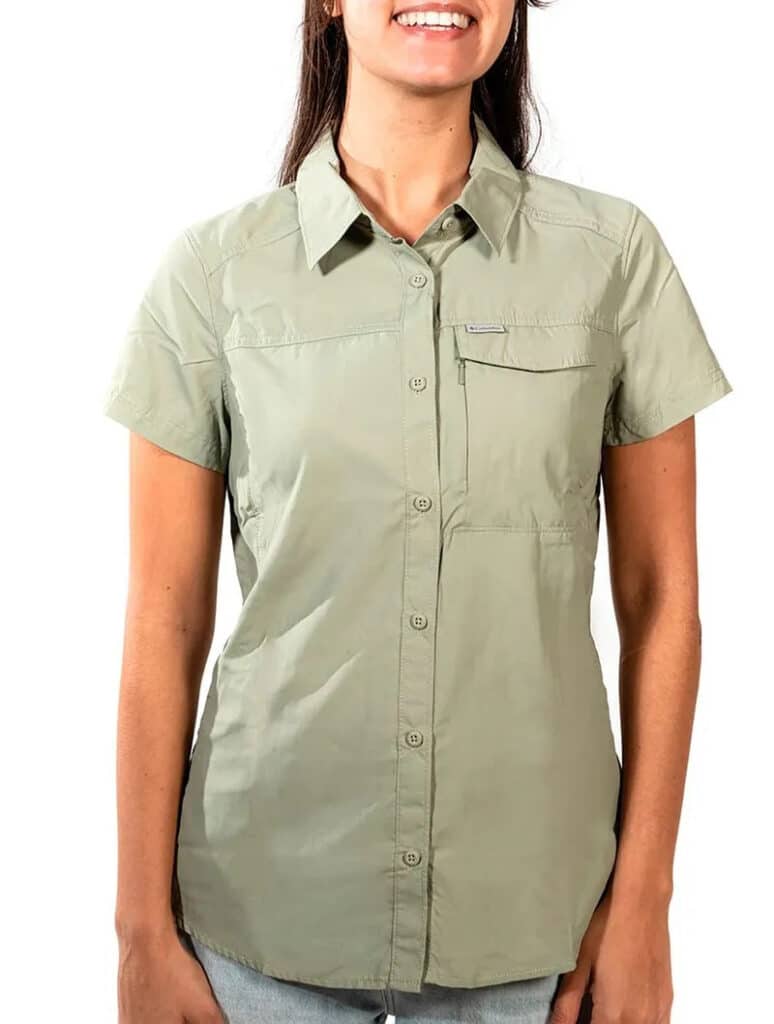 Pessoa vestindo uma camiseta Columbia verde-clara de manga curta, com botões, gola e bolso no peito, sorrindo em frente a um fundo branco.