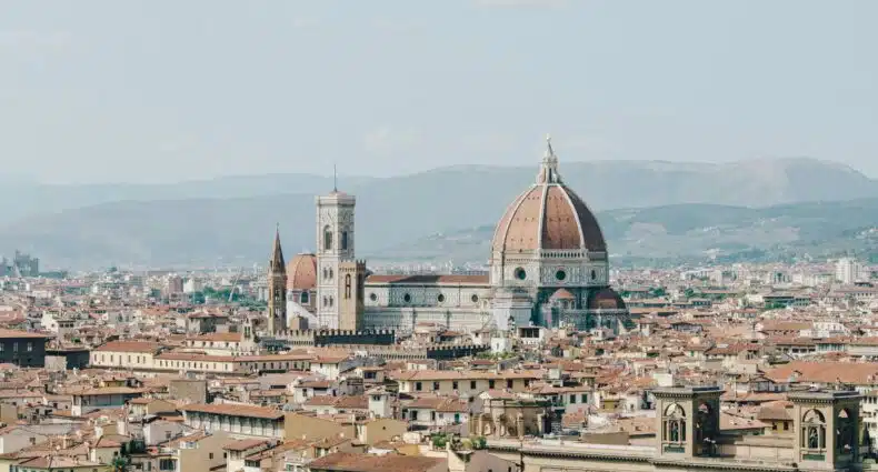 Vista aérea de Florença, Itália, mostrando a cúpula da Catedral de Florença e edifícios ao redor com montanhas ao fundo. A foto ilustra o post de o que fazer em Florença.