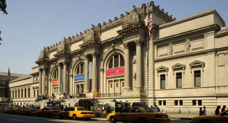A imagem mostra o exterior do Metropolitan Museum of Art de estilo clássico com táxis amarelos enfileirados na frente em um dia ensolarado. Imagem para ilustrar post sobre museus em Nova York.