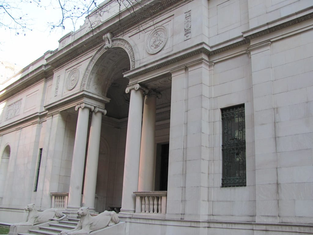Exterior do Morgan Library & Museum com colunas, um arco central e duas estátuas de leões ladeando os degraus de entrada.