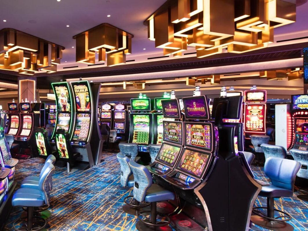 Salão de jogos de cassino no The STRAT, com fileiras de máquinas caça-níqueis coloridas, cadeiras azuis acolchoadas e modernas luzes geométricas no teto. Esse é um dos melhores cassinos em Las Vegas.