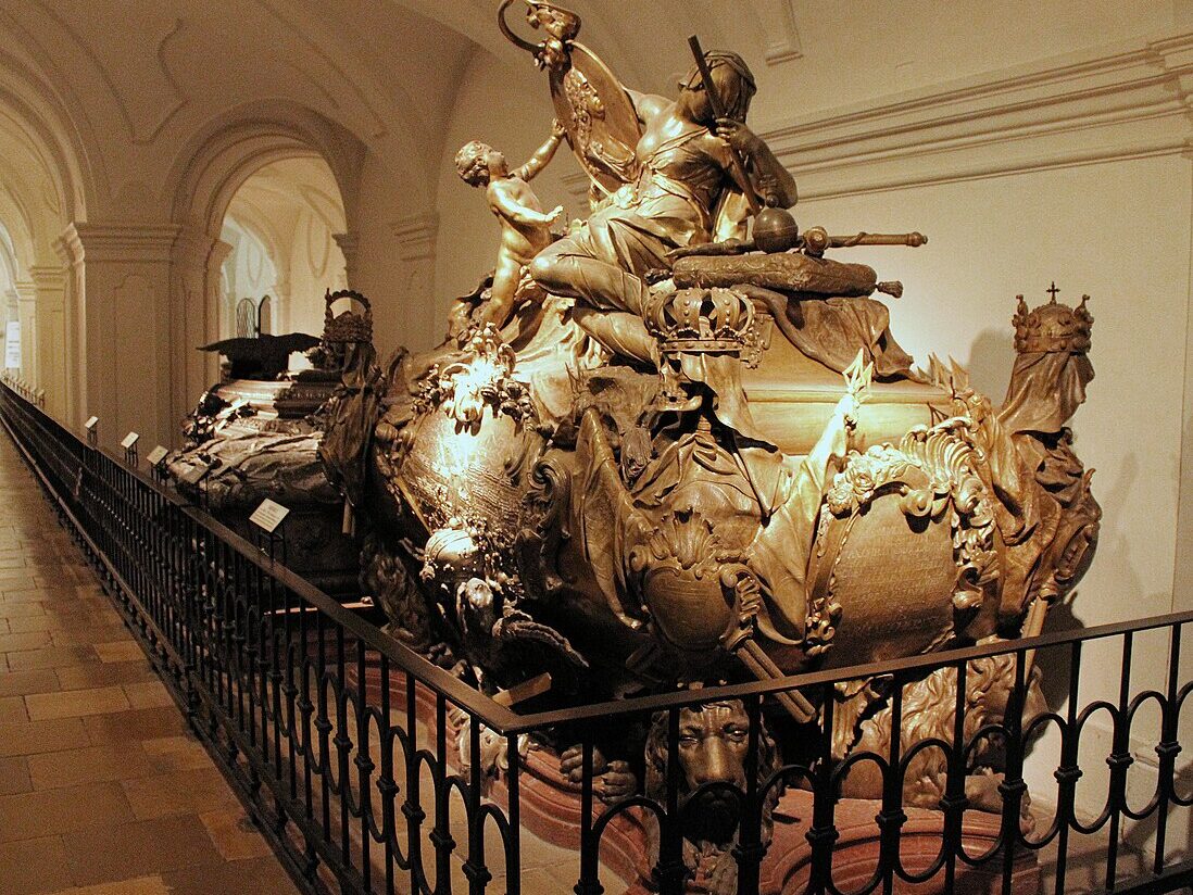 Sarcófago Cripta Imperial. Ele é ornamentado com esculturas complexas, incluindo figuras e coroas, exposto em um corredor de museu com pouca iluminação. A foto ilustra o post de o que fazer em Viena.