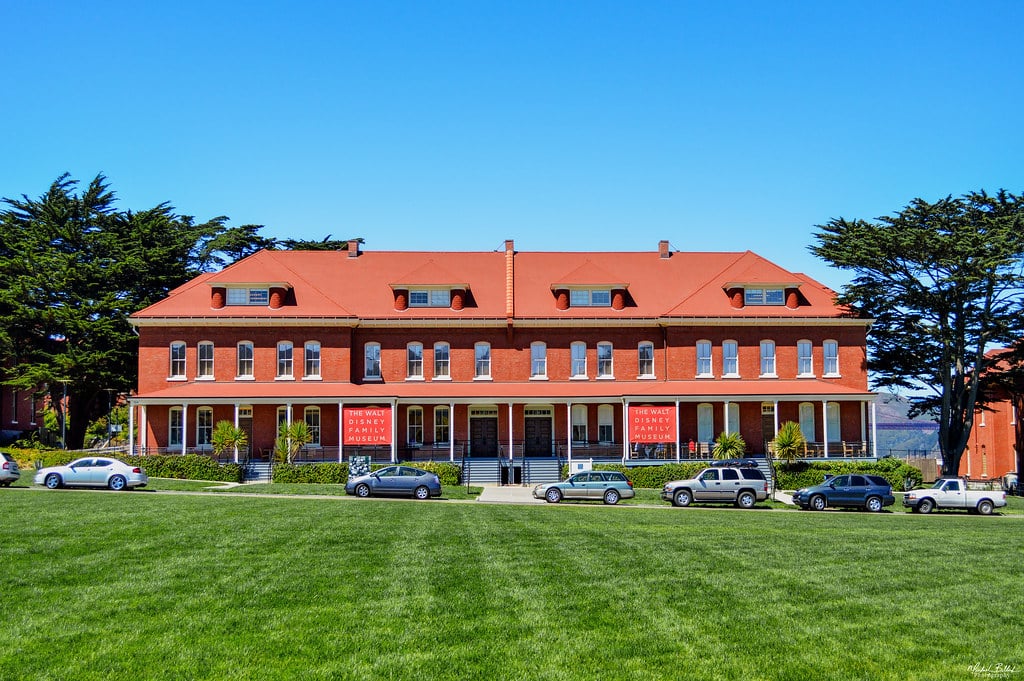 Walt Disney Family Museum com várias janelas e faixas vermelhas, está posicionado atrás de um campo gramado.
