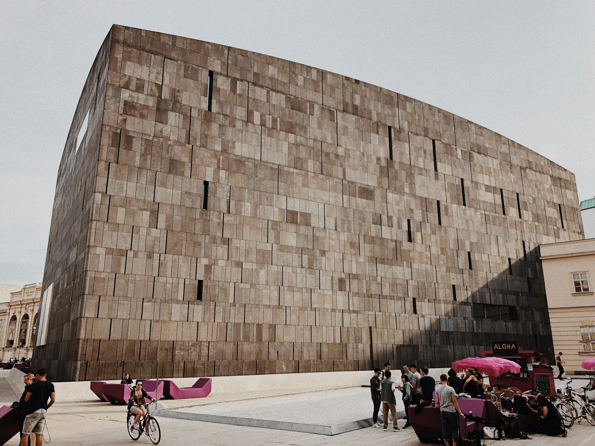 Museu de Arte Moderna no Museumsquartier. É um grande edifício moderno de concreto com formato cúbico, com pessoas caminhando e sentadas em bancos em primeiro plano. A foto ilustra o post de o que fazer em Viena.