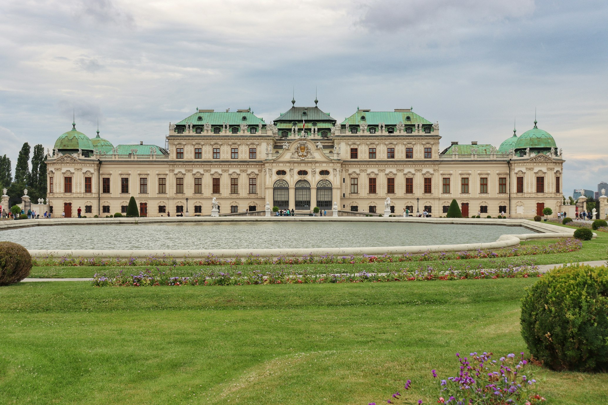 Palácio Belvedere com cúpulas verdes, grande pátio central e uma fonte decorativa em primeiro plano sob um céu nublado. Ele está na lista de o que fazer em Viena.