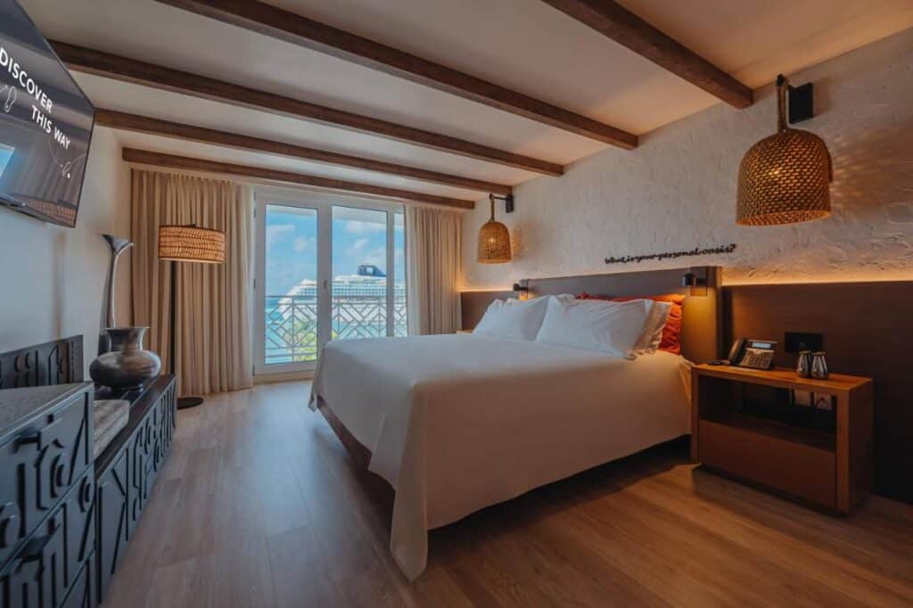 Um quarto moderno do Renaissance Wind Creek Aruba Resort com uma cama king-size, vigas de madeira, janelas grandes, TV montada na parede e iluminação decorativa.