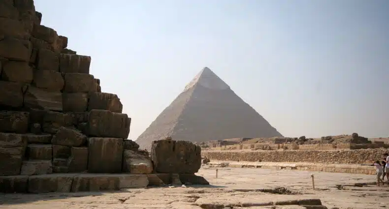 Uma vista das pirâmides de Gizé, no Cairo, com um close-up de uma pirâmide em primeiro plano e da Grande Pirâmide à distância.