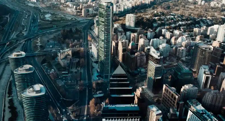 Vista aérea de uma paisagem urbana com arranha-céus altos, em Santiago com um rio com pontes e estradas urbanas cercadas por edifícios residenciais. Representa pontos turísticos de Santiago.