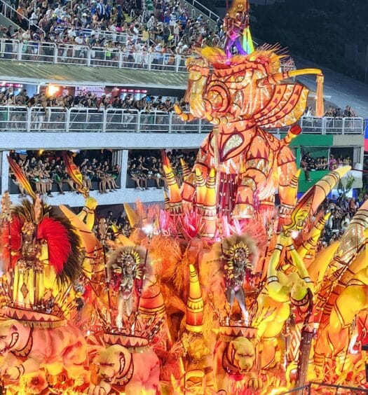 Um vibrante carro alegórico com esculturas de elefantes e dançarinos, cercado por uma multidão animada sob luzes brilhantes no Rio de Janeiro. Imagem para ilustrar post sobre o que fazer no Carnaval.