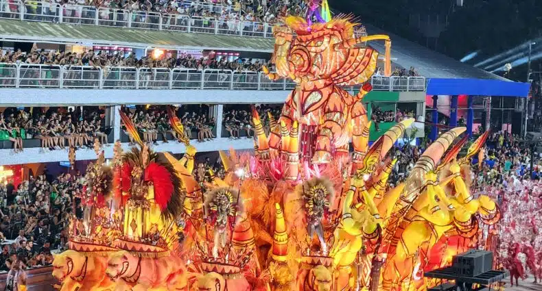 Um vibrante carro alegórico com esculturas de elefantes e dançarinos, cercado por uma multidão animada sob luzes brilhantes no Rio de Janeiro. Imagem para ilustrar post sobre o que fazer no Carnaval.