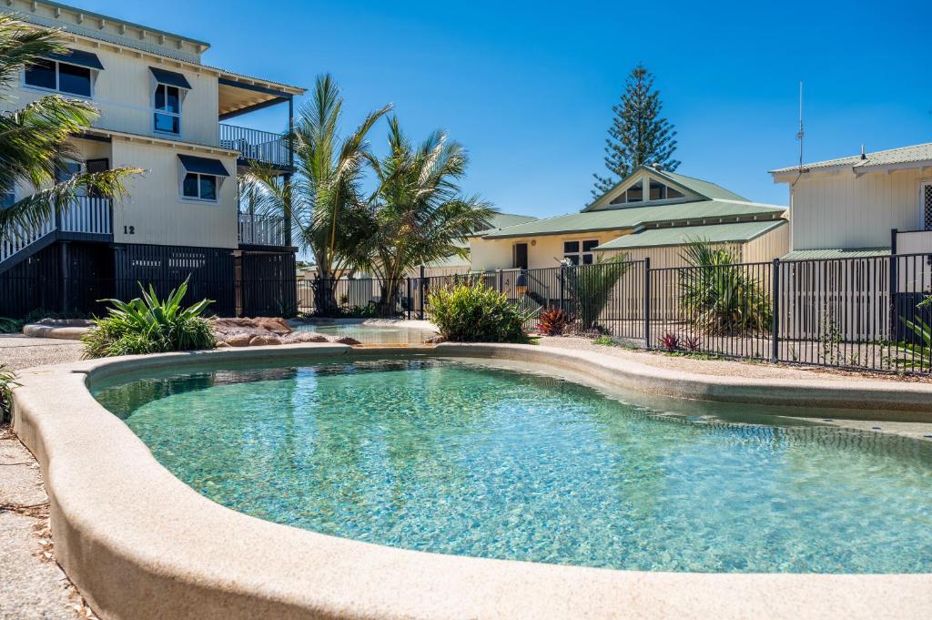 Uma tranquila piscina ao ar livre no E.V. - Eurong Beach Villa com águas cristalinas, cercada por palmeiras e edifícios sob um céu azul claro.