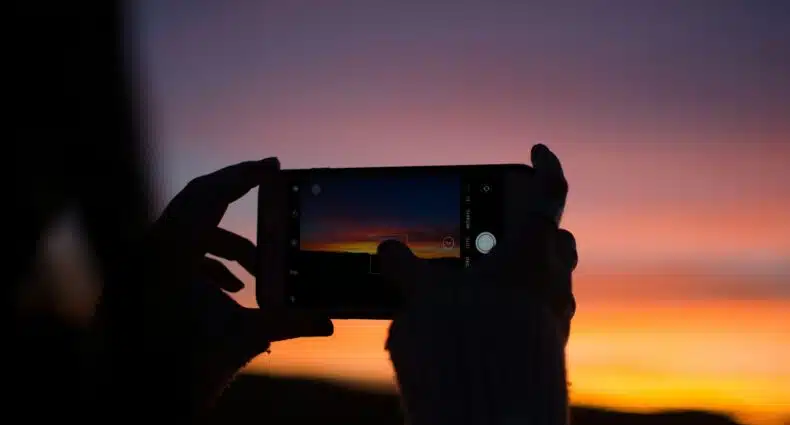 Uma pessoa tira uma foto do pôr do sol com um smartphone, capturando tons vibrantes de laranja e roxo no céu de Capilla del Monte, Córdoba, para ilustrar o post de eSim Argentina