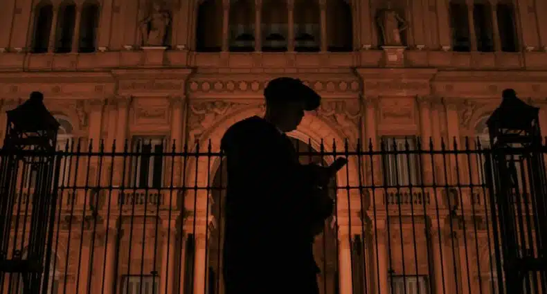 Silhueta de uma pessoa usando um telefone em frente a um edifício histórico iluminado à noite, com arquitetura ornamentada e um relógio no topo, para ilustrar o post de eSIM Buenos Aires