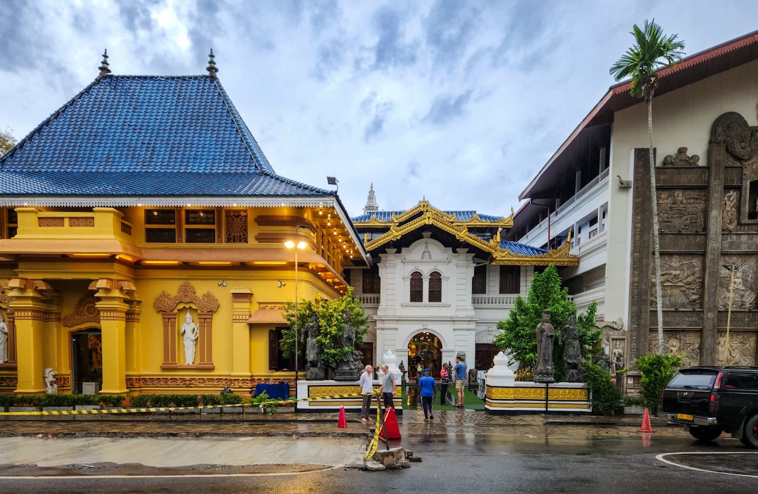 Um complexo de templos coloridos com telhados ornamentados em dourado e azul, com estátuas e detalhes intrincados, sob um céu nublado, em Templo de Gangaramaya. Representa o que fazer no Sri Lanka.