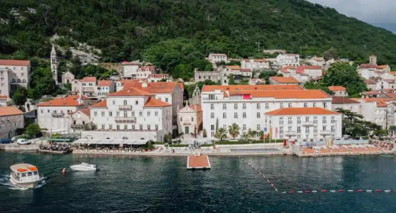 Heritage Grand Perast By Rixos, em Perast, com telhados vermelhos, perto de uma encosta coberta de árvores e um pequeno cais ao longo da água; um barco pode ser visto nas proximidades, para representar hotéis em Montenegro.