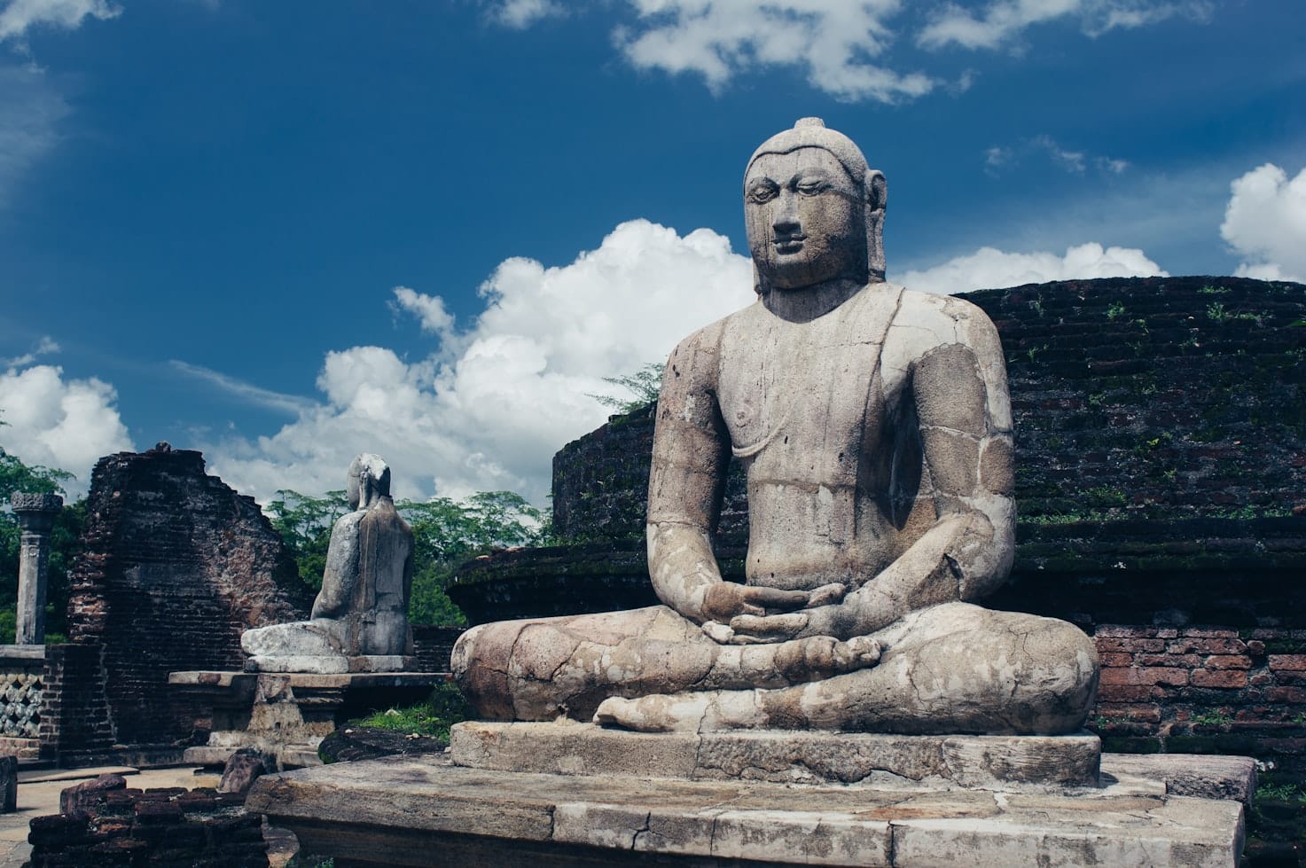 Antigas estátuas de pedra de Buda em pose meditativa em um local histórico com céu azul e nuvens dispersas acima, em Polonnaruwa. Representa o que fazer no Sri Lanka.