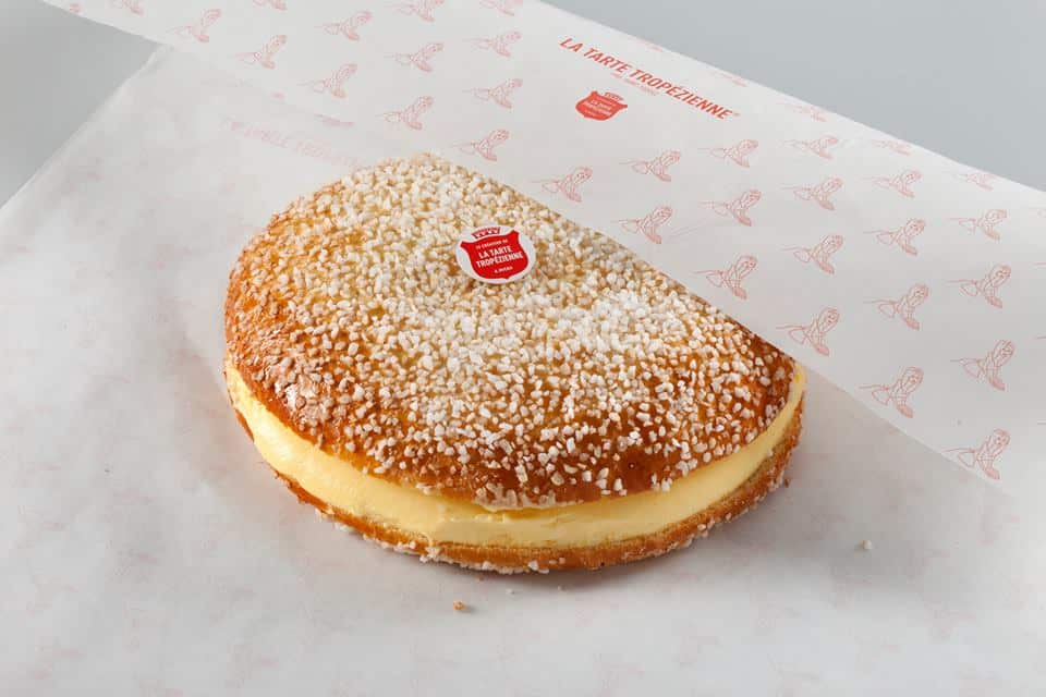 Massa redonda polvilhada com açúcar, recheada com creme light, parcialmente embrulhada em papel branco com etiqueta vermelha.