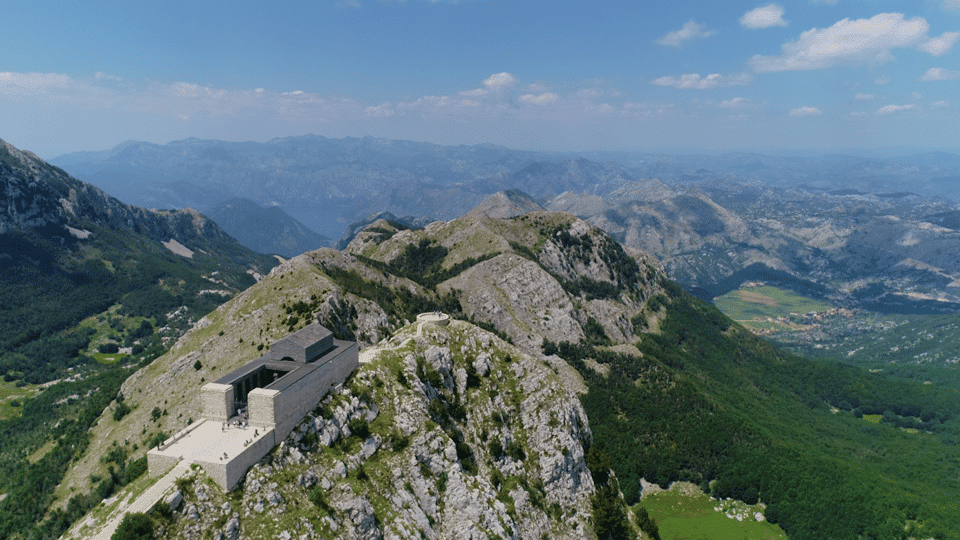 Vista aérea de um edifício de pedra, o Mausoléu de Njegoš no topo do Monte Lovcen, em uma montanha rochosa com vastos vales verdes e cadeias de montanhas distantes sob um céu azul, para representar o que fazer em Montenegro.
