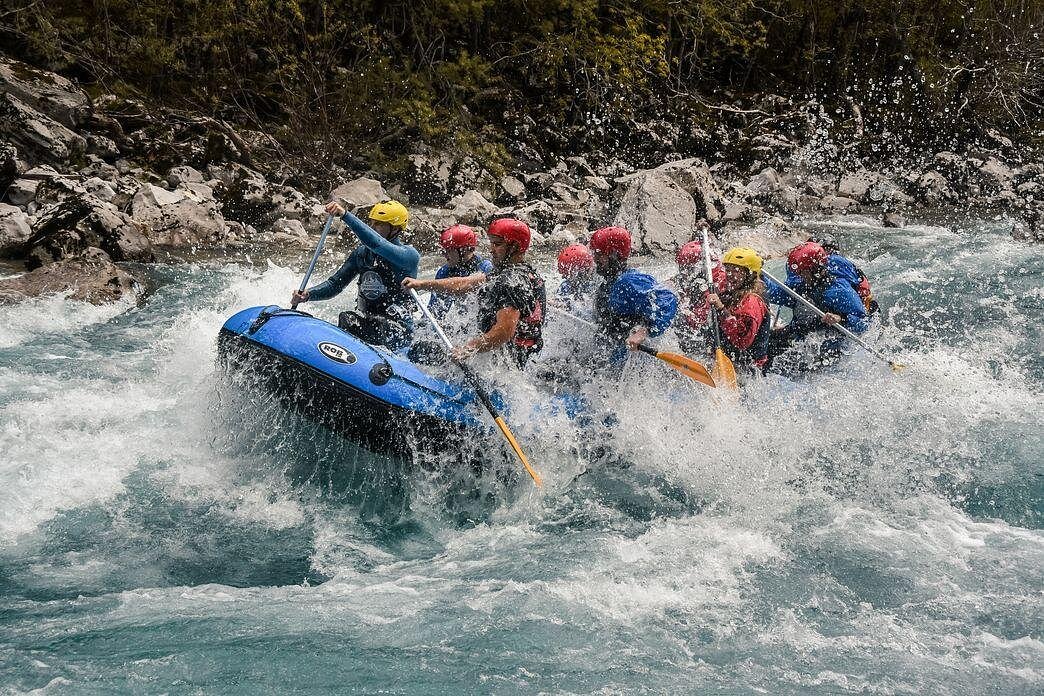 Um grupo de pessoas usando capacetes está praticando rafting em um bote inflável azul, navegando por corredeiras rochosas no rio Tara, em Montenegro.