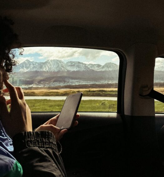 Pessoa segurando um telefone, sentada em um carro. Do lado de fora da janela, uma cadeia de montanhas é visível sob um céu parcialmente nublado que ilustra o post de eSIM Ushuaia