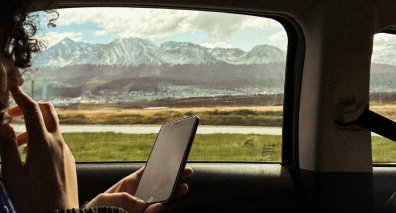 Pessoa segurando um telefone, sentada em um carro. Do lado de fora da janela, uma cadeia de montanhas é visível sob um céu parcialmente nublado que ilustra o post de eSIM Ushuaia