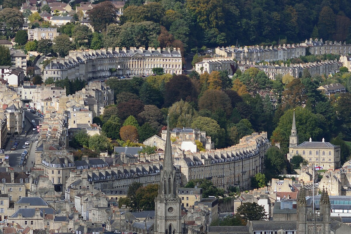 Vista aérea de Bath, com edifícios curvos, igrejas e vegetação ao redor em uma encosta. A foto foi tirada do Alexandra Park, do alto de Beechen Cliff.