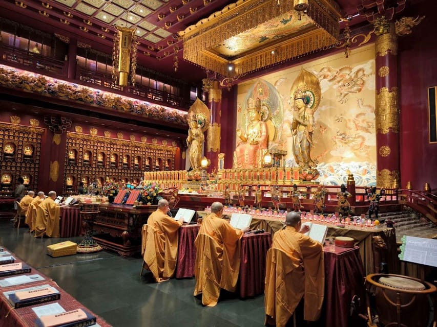 Monges em vestes amarelas conduzindo uma cerimônia em um templo ornamentado com grandes estátuas douradas e decorações complexas.