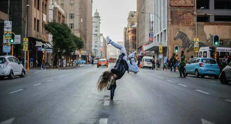 Uma pessoa dançando break com uma das mãos no meio de uma rua da cidade, com prédios, carros e pessoas ao fundo. Que pode ser visitado com o eSIM Johanesburgo.