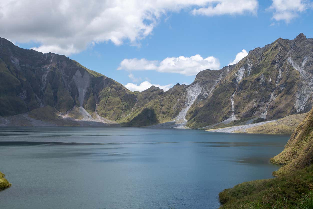 Um lago calmo é cercado por montanhas íngremes e verdes sob um céu parcialmente nublado. Essa é uma das dicas de o que fazer nas Filipinas.