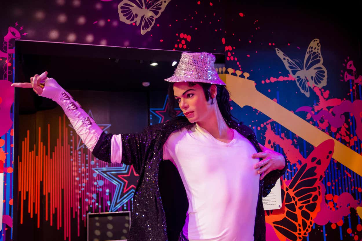 Figura de cera do Michael Jackson vestida com chapéu e luvas brilhantes, posando contra um fundo colorido com estrelas e borboletas no Madame Tussauds de Singapura.