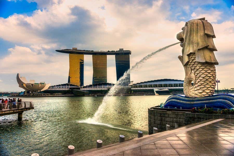 A estátua do Merlion em Singapura jorra água, com o Marina Bay Sands e o Museu ArtScience ao fundo. Ilustra o que fazer em Singapura.