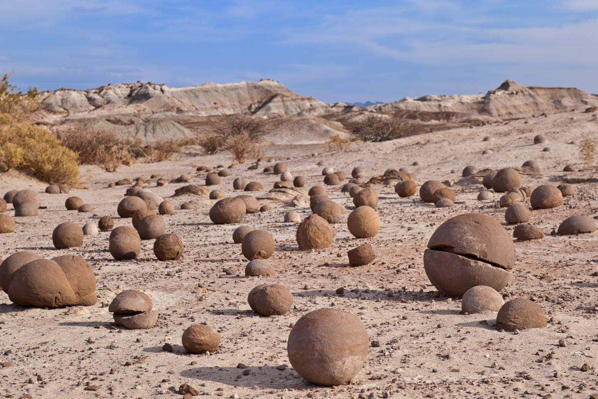 Formações rochosas esféricas no Parque Provincial de Ischigualasto espalhadas por uma paisagem desértica com colinas ao fundo sob um céu azul.